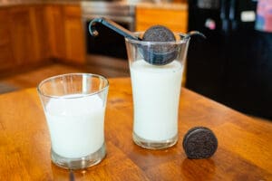 A glass of milk and cookie in front of a cup.