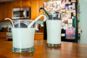 Two glasses of milk on a table in front of a wall.