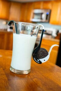 A glass of milk with cookies on the spoon.