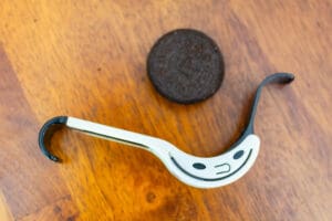 A spoon with a smiley face on it next to an oreo cookie.