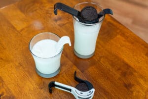 A wooden table with two glasses and an oreo cookie in the glass.