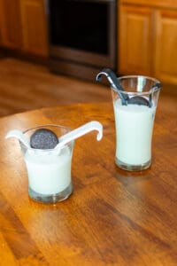 Two glasses of milk with a cookie in the middle.