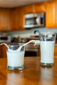 Two glasses of milk and a cookie on the table.