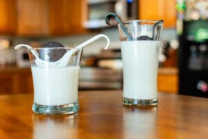 Two glasses of milk on a table with spoons.