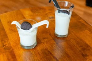 Two glasses of milk with a cookie on top.