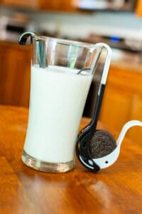 A glass of milk next to an oreo cookie.