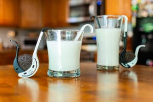 A wooden table with two glasses of milk and spoons.